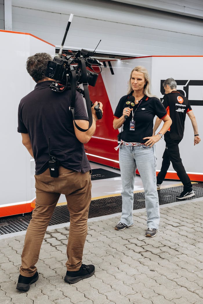 Camera crew interviews a woman at a raceway event outdoors.